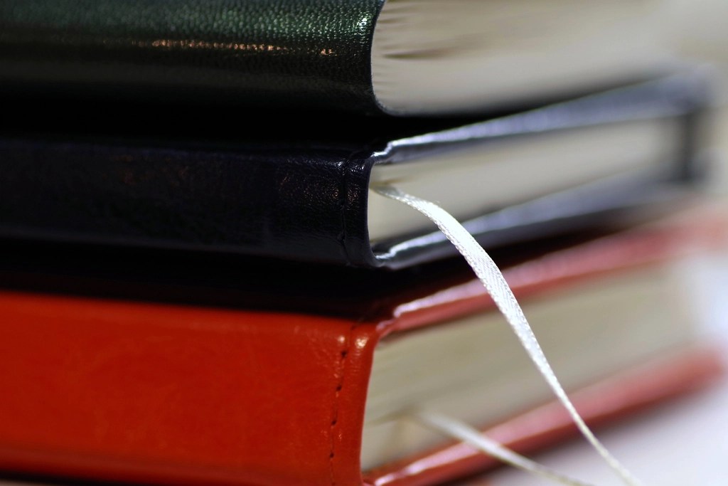 A close-up image of stacked notebooks in different colors, showcasing their spines and bookmarks.