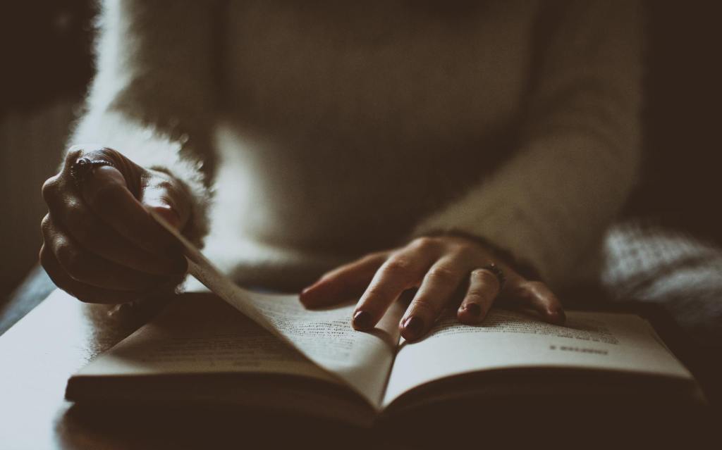 A person's hands gently turning the pages of an open book, with a soft focus background.
